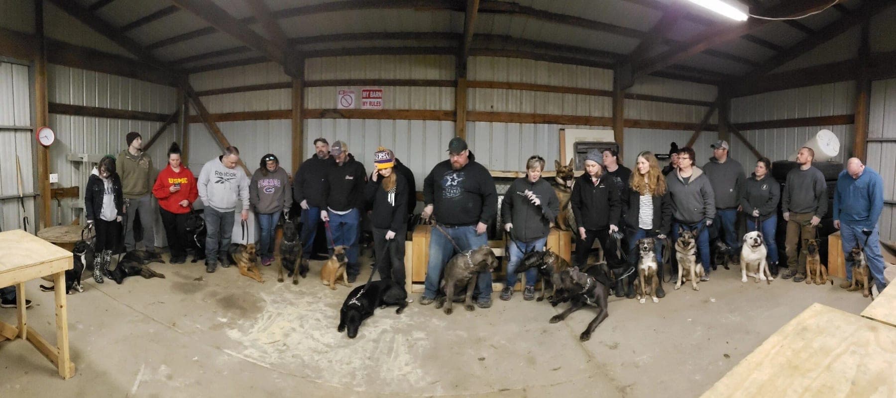 A full class of handlers and their dogs standing together inside the barn